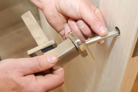 Dłoń wyciąga metalowy trzpień z klamki okiennej, pokazując jak wyjąć trzpień z klamki okiennej.