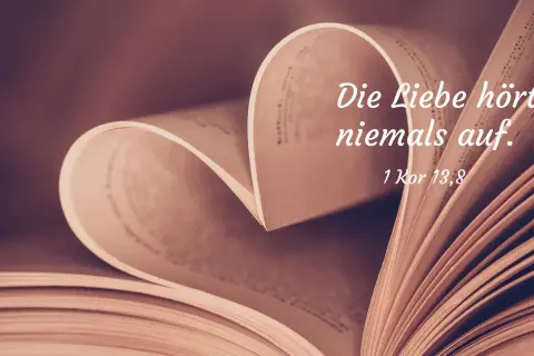 Ein aufgeschlagenes Buch formt ein Herz. Darauf steht: "Die Liebe hört niemals auf. 1 Kor 13,8". Bibelzitate über Liebe und Ehe.