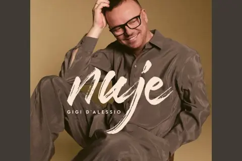 Gigi D'Alessio sorride, con la mano tra i capelli. Sulla sua camicia, la scritta "Nuje". Chissà cosa ci spiegate cherè.