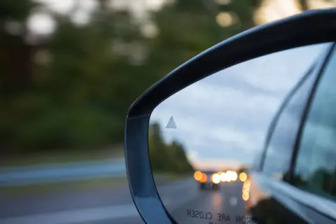 Specchietto retrovisore con indicatore del sistema side assist attivo, riflette la strada e le luci delle auto.