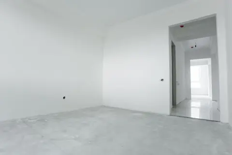 Habitación vacía con paredes blancas y suelo de cemento. El yeso aguanta el calor, preparándose para un nuevo hogar.