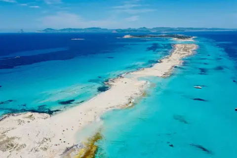 Arena blanca y aguas turquesas en la mejor playa de Formentera. Un paraíso con barcos y gente disfrutando del sol.