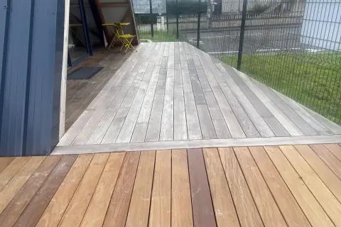 Terrasse en bois avec une partie grise, signe qu'il faut enlever le saturateur bois. Une table et une chaise jaunes sont visibles.