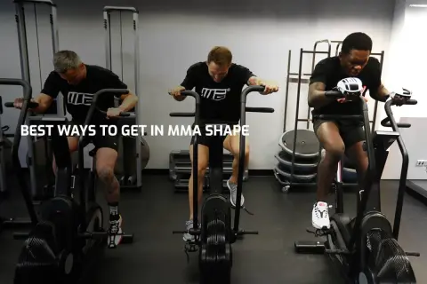 Three men with impressive fighters physique train on air bikes in a gym, showcasing their dedication to peak physical condition.