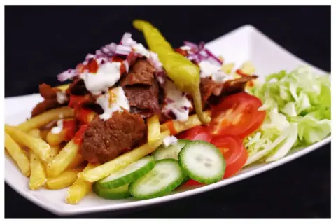 En tallrik med kebab, pommes frites, tomater, gurka, sallad och en stark chili. Perfekt för dig som söker ett gott kebabsås recept.