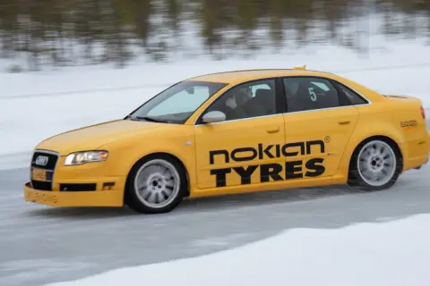 Żółty Audi S1 Quattro z napisem "Nokian Tyres" śmiga po lodowym torze. Kierowca pokazuje kciuk w górę.
