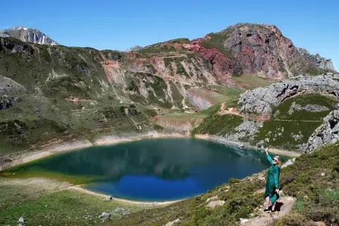 Mujer en la ladera disfruta de las vistas de un lago azul rodeado de montañas, ideal para rutas en Somiedo.