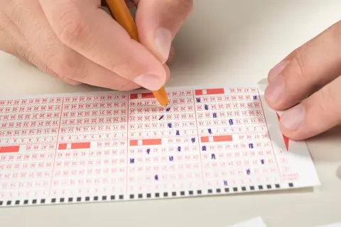 Ręka zaznacza liczby na kuponie lotto, zastanawiając się, ile do wygrania w mini lotto.