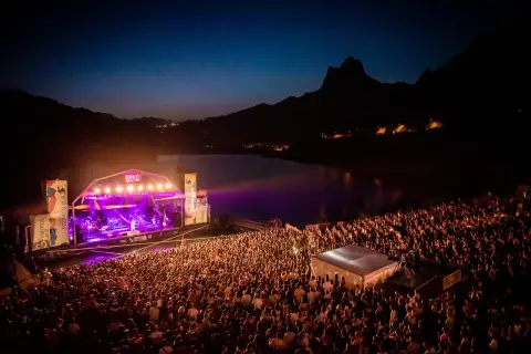 Gran concierto nocturno en el Pirineos Sur. Un mar de gente disfruta de la música bajo un cielo estrellado y montañas.