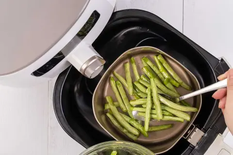 Gröna bönor läggs i en korg för en varm luft ugn.