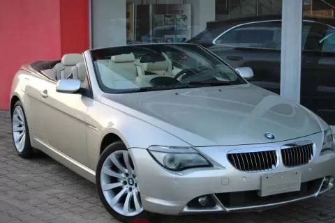 Srebrny kabriolet BMW E64 z beżowym wnętrzem stoi przed salonem samochodowym.
