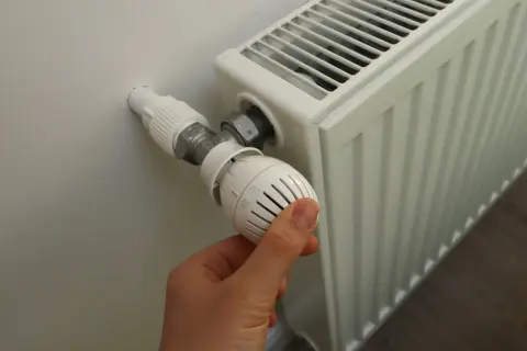 Ręka reguluje termostat grzejnika, gdy zaczynają grzać w blokach.