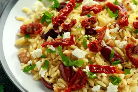 Pyszna sałatka z makaronu orzo, suszonych pomidorów, oliwek, sera feta i świeżej bazylii.