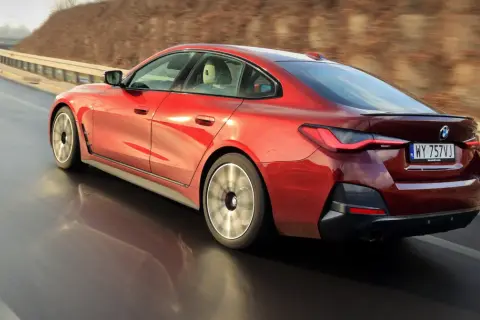 Czerwone BMW 4 Gran Coupé pędzi po zakręcie drogi, ukazując dynamiczną sylwetkę i sportowe felgi.