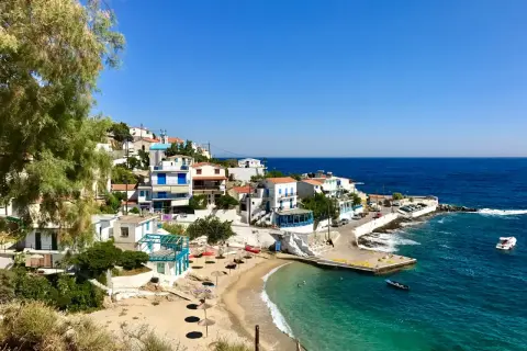 En pittoresk kustby på Ikaria, Grekland, med vita hus, en sandstrand och turkost vatten.