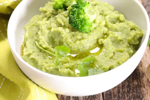 Un bol de purée de brocolis onctueuse, garnie de fleurettes de brocolis et d'un filet d'huile d'olive.