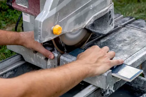 Hands guide a tile across a wet saw, demonstrating how to cut tile that is already installed.