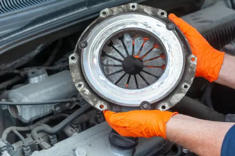 Mains gantées d'orange tenant un embrayage usé, signe d'un embrayage qui patine. Réparation automobile.