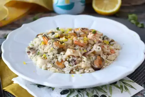 Pyszne risotto z owocami morza, udekorowane skórką cytrynową i ziołami, na białym talerzu.