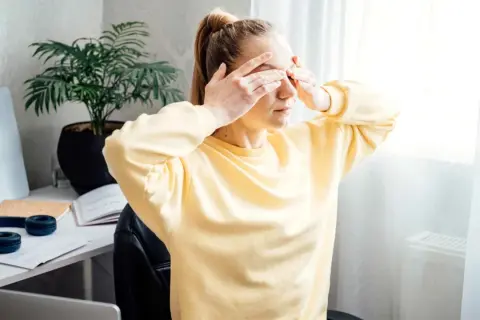 Une jeune femme, le visage marqué par la tension oculaire et le stress, se couvre les yeux.
