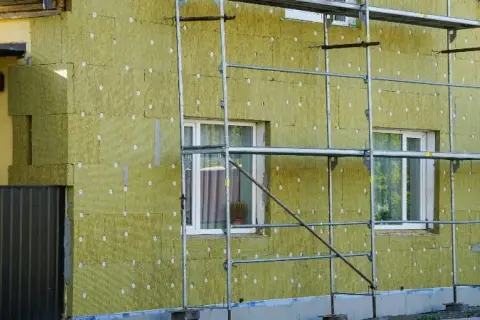 Budynek ocieplany wełną mineralną, widoczne rusztowania i okna. Tak powstaje wełna, która chroni dom.