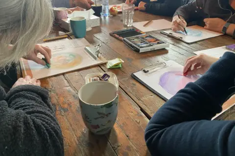 Creatieve workshop voor hsp mensen. Ze tekenen met pastelkrijt op papier, omringd door kopjes en kleurpotloden.