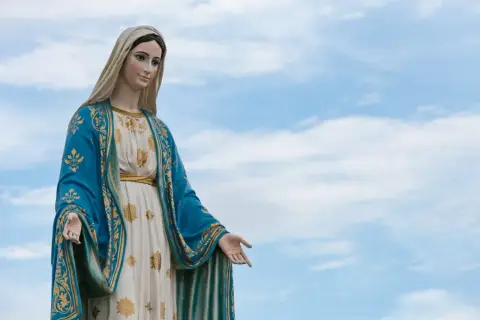 Kamienna figura Matki Bożej w błękitnym płaszczu ze złotymi zdobieniami, jakby wznosiła się do nieba podczas litanii do Matki Bożej.
