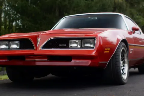 Röd Pontiac Trans Am från 70-talet, med sina karaktäristiska dubbla strålkastare och en ikonisk grill.