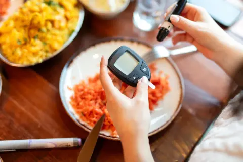 Mani che usano glucometro e lancetta. Piatto con carote grattugiate. Cosa non mangiare la sera prima delle analisi del sangue.