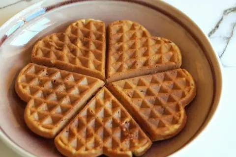 Herzförmige Waffeln ohne Zucker, goldbraun gebacken, liegen auf einem Teller.