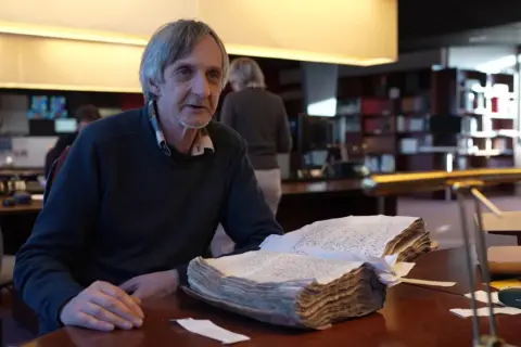 Un homme consulte un livre ancien, peut-être une source pour les meuse archives en ligne.