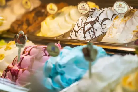 Verschiedene Eissorten in einer Auslage, darunter ein cremiges gelbes Eis, Stracciatella und ein fruchtiges Eis.