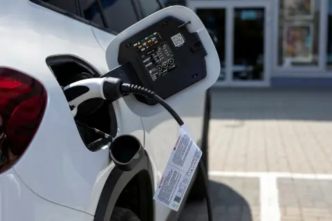 Biały samochód podłączony do ładowania. To przyszłość motoryzacji, czyli przerabianie samochodów na elektryczne.
