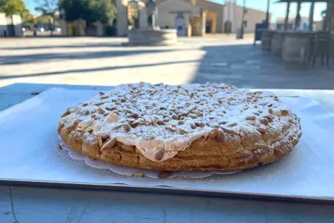 Tarte aux pignons de Gruissan, saupoudrée de sucre glace, sur une table ensoleillée.