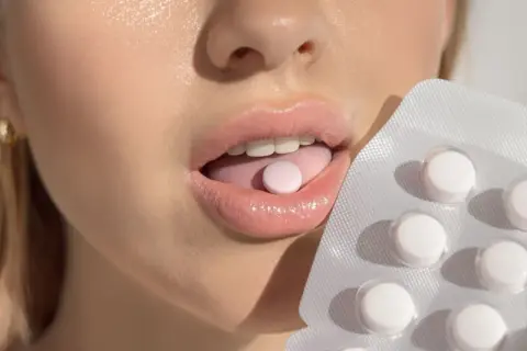 Probiotyk na nieprzyjemny zapach z ust. Kobieta kładzie tabletkę na języku, obok opakowanie.