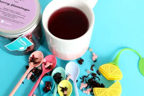 Kolorowa kompozycja z herbatą dla dzieci "Berry Flamingo". Sześć małych łyżeczek z suszem owocowym, kubek z naparem i urocze akcesoria do parzenia.