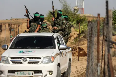 Uzbrojeni bojownicy Hamas w zielonych opaskach na głowach siedzą na białej toyocie, gotowi do akcji.