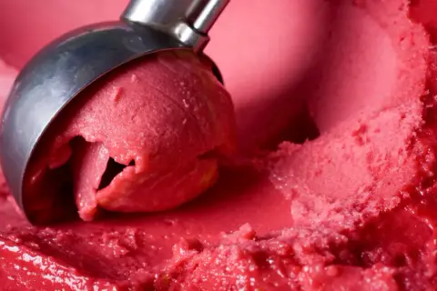 Ein Löffel nimmt eine Kugel leuchtend rotes Eis auf. Es sieht aus wie ein köstliches Eis mit Ei, das auf der Zunge zergeht.