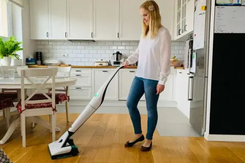 Kobieta sprząta kuchnię nowoczesnym odkurzaczem Vorwerk.