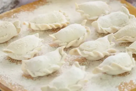 Surowe pierogi, gotowe do gotowania, posypane mąką. Idealne na domowy obiad, zgodnie z tradycyjnym ciasto na pierogi przepisem.
