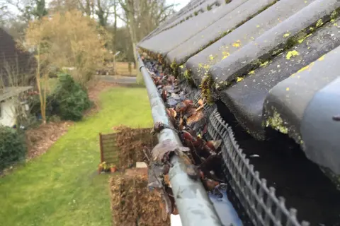 Herbstlaub und Moos verstopfen die Dachrinne. Zeit für die Dachrinne reinigen, um Wasserschäden zu vermeiden.