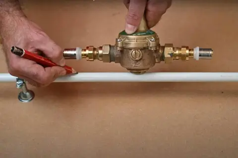 Ajustement d'un réducteur de pression pour comment augmenter la pression d'eau. Un homme marque un tuyau avec un crayon.