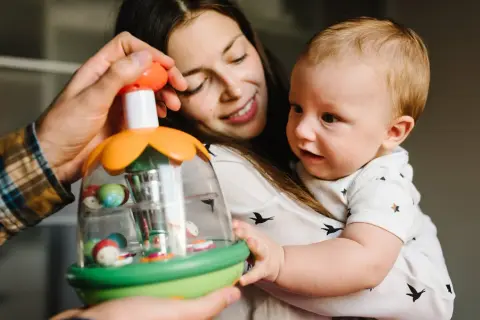 Mama i tata pokazują dziecku zabawkę. Maluch, choć nie jest jeszcze dwulatkiem, z zaciekawieniem kręci głową, obserwując kolorowe kulki.