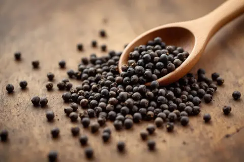 Une cuillère en bois déborde de grains de poivre noir, posée sur une surface en bois. Le poivre est-il bon pour la santé ? Ces petites baies pourraient bien l'être.