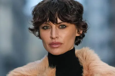 Ein modischer Pixie Cut mit feinem Haar betont die grünen Augen einer Frau in einem Pelzmantel.