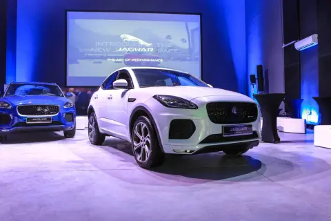 Biały i niebieski Jaguar E-Pace na prezentacji. Na ekranie w tle logo Jaguara i napis "Introducing the new Jaguar E-Pace".