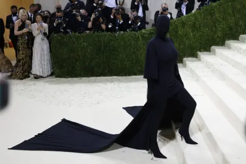 Kim Kardashian al Met Gala, un'apparizione misteriosa in nero totale, con un abito che si estende sul tappeto bianco.