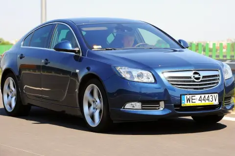Niebieski Opel Insignia 1.6 Turbo pędzi po drodze. Kierowca wpatrzony w horyzont.