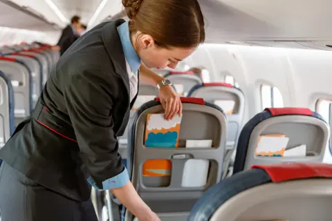 Uśmiechnięta stewardessa przygotowuje kabinę samolotu, układając materiały w kieszeniach foteli.