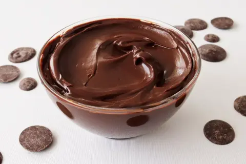 Un tazón de deliciosa crema de chocolate, con trozos de chocolate esparcidos alrededor.